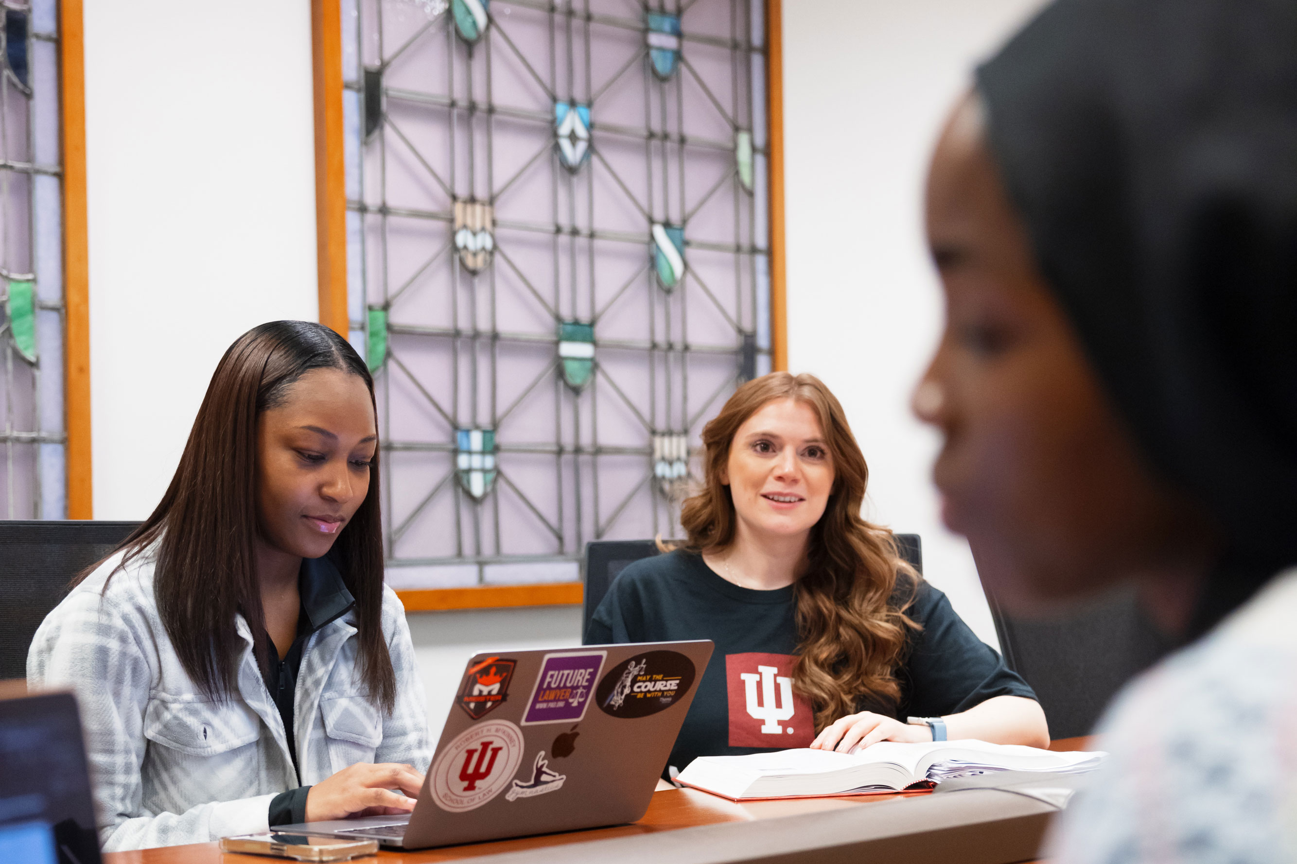 three students around a table with one student on her laptop